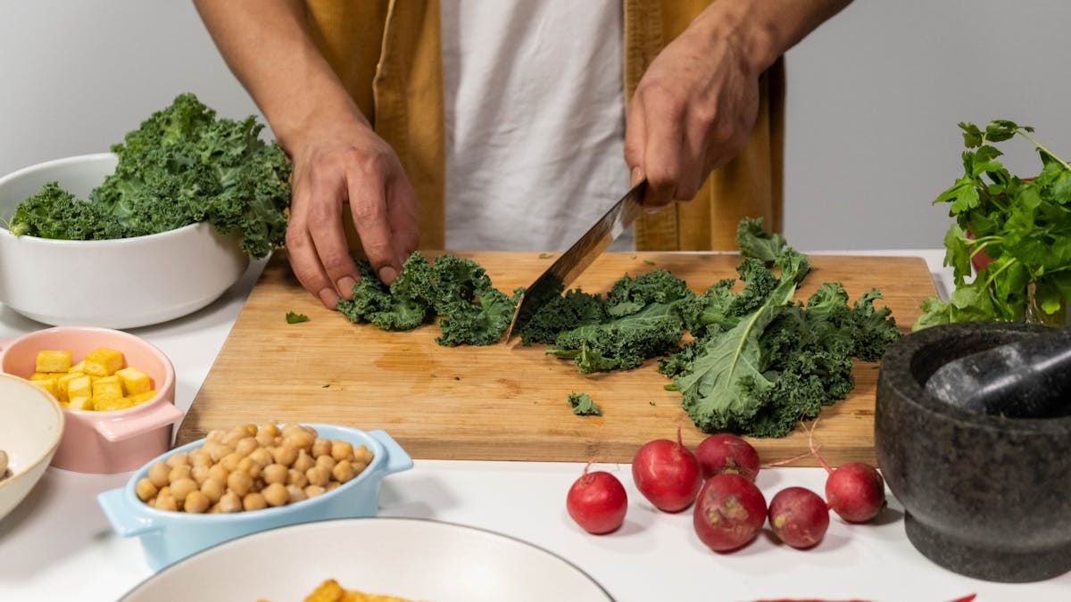 A person chops fresh kale surrounded by vibrant vegetables for a healthy meal preparation in a kitchen.